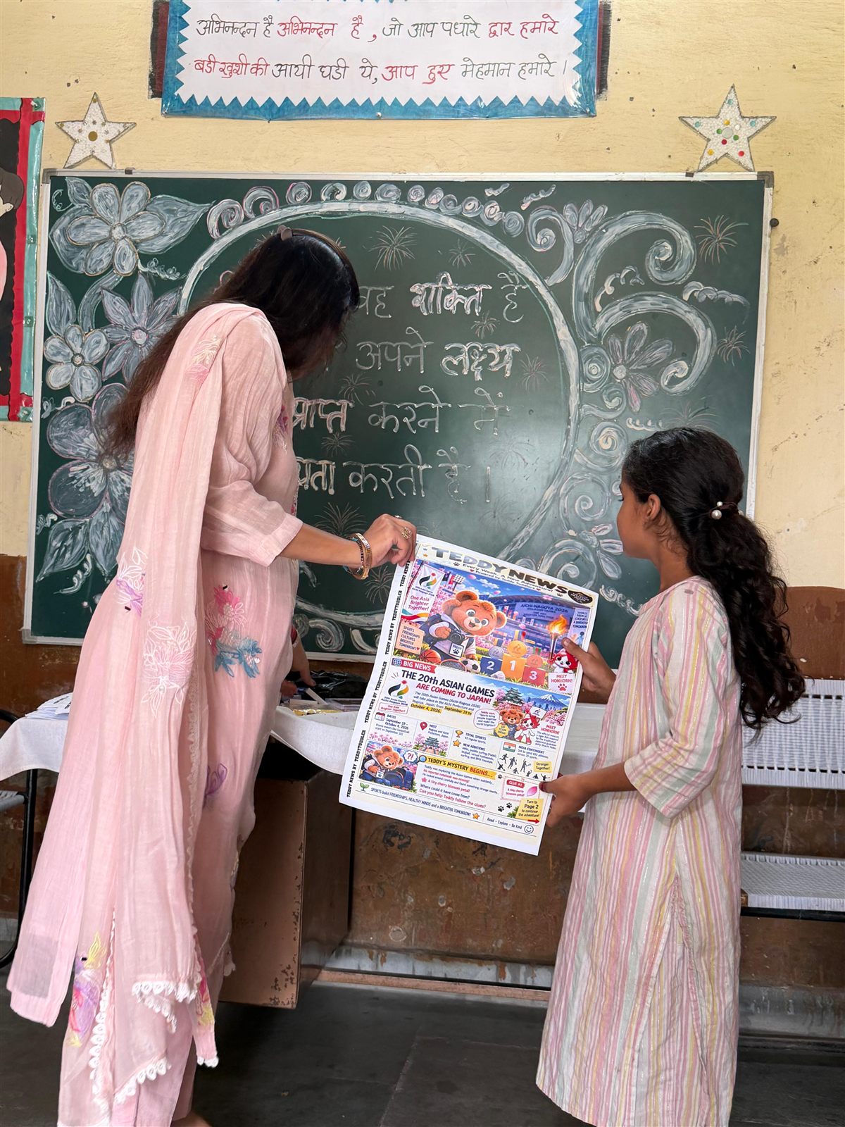 A Teddy News team member showing a young girl her new Teddy News issue in a classroom